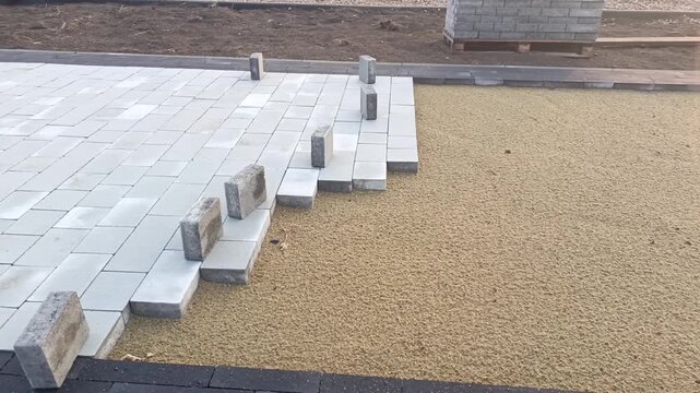Road paving with concrete paving stones, pallets of paving blocks and sand on construction site, pavement installation and infrastructure construction.
