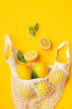 Lemons with green leaves in reusable mesh bag, vibrant citrus composition on yellow background seen from above. Sustainable shopping, natural produce and eco living concepts suit lifestyle campaigns.
