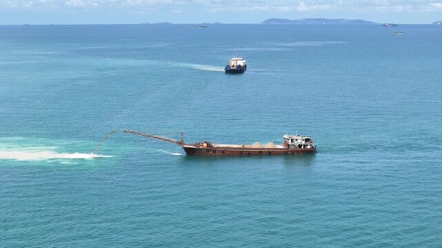 Sand dredging ship discharging sand into the sea for land reclamation project. Coastal engineering and marine infrastructure development. Industrial vessel working on artificial island construction.