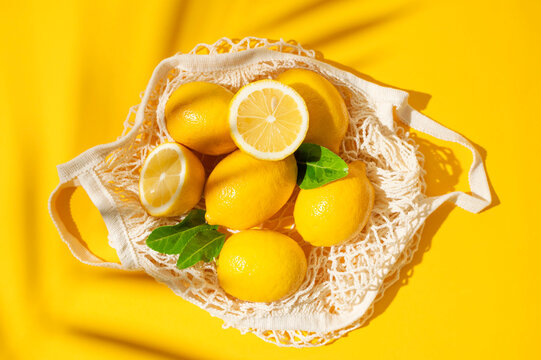 Lemons with green leaves in reusable mesh bag, vibrant citrus composition on yellow background seen from above. Sustainable shopping, natural produce and eco living concepts suit lifestyle campaigns.