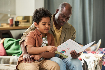 African American senior man reading book with child boy, guiding learning and bonding at home....