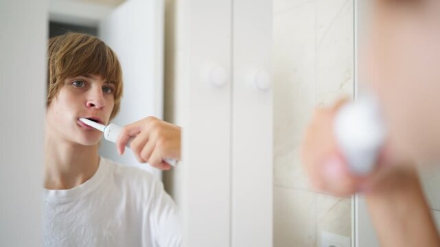 Daily morning routine of teenager brushing teeth with an electric toothbrush in front of mirror, emphasizing dental care and personal hygiene for maintaining healthy, clean teeth