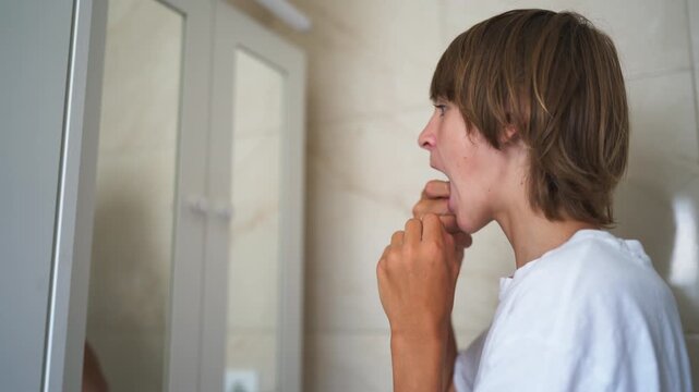Responsible teenage boy using dental floss in front of a bathroom mirror, taking preventive care of his teeth and practicing good oral hygiene to support long-term dental health.