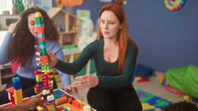 Woman steadies a tall colorful building block tower and guides a boy's hands stacking bricks in a playroom building; nurturing learning.