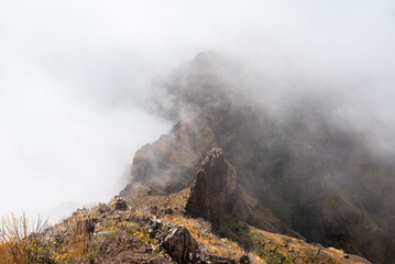 Fototapeta premium A rocky ridge peak wrapped in swirling mist on the PR1 trail, Madeira