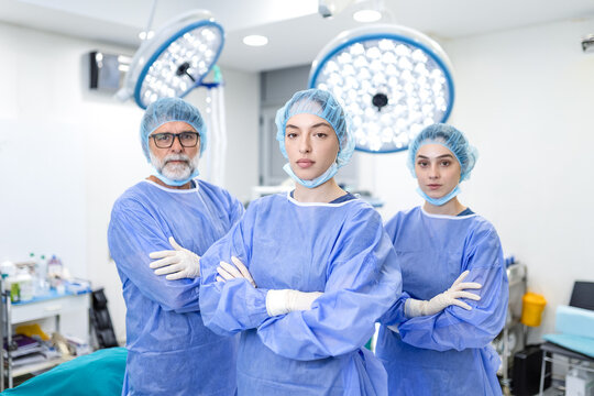 Medical team in operating room. Professional surgeons standing with crossed arms, Hospital and surgery concept. Doctors wearing blue scrubs and surgical caps ready for operation.