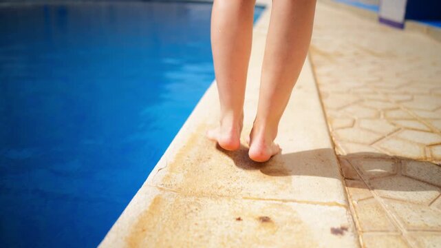 Barefoot woman's legs walking alongside swimming pool on sunny summer day.Concept relaxing vacation and wellness lifestyle with low-angle view