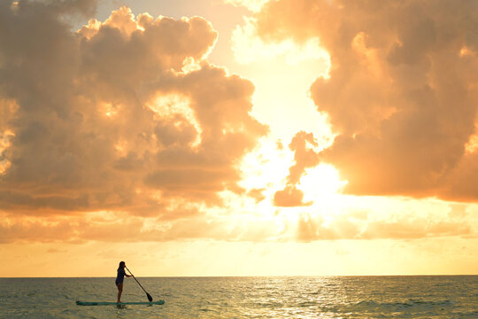 Lone woman paddleboarding towards a golden sunset