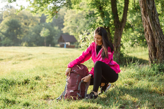Young woman opening backpack on meadow near forest