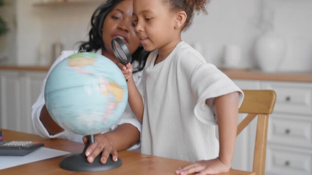 Mother or teacher showing globe to little black girl, geography lesson in school. Preschooler child enjoy education and homeschooling, traveling and exploring world, choosing location for holidays