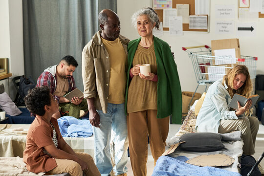 Senior Caucasian woman and Black man standing in shelter, supporting displaced families during crisis. Suitable for humanitarian aid, community support, social care campaigns