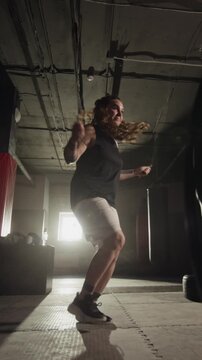 Vertical of Young Caucasian woman jumping rope during intense cardio workout in dark gym. Perfect for fitness brand advertisements and motivational sports content