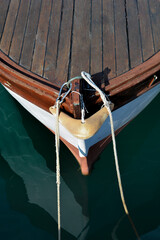 Fototapeta premium A high angle vertical shot of a traditional wooden boat bow with mooring lines and a metal karabiner floating on calm sea water