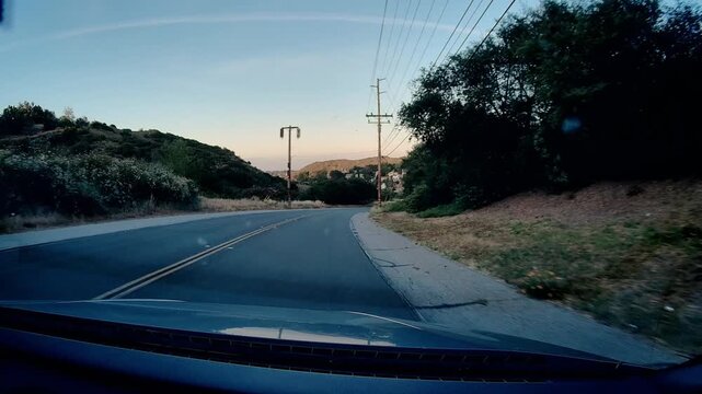 Dashcam view Mulholland Highway winding road drive Los Angeles hills power lines. Scenic route Southern California clear blue sky day, vehicle perspective empty road.