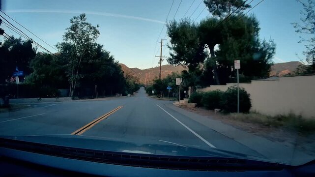 Dashcam view of Mulholland Hwy. winding road through scenic mountainous landscape of Southern California, featuring clear blue sky, green trees, even utility poles alongside pavement.