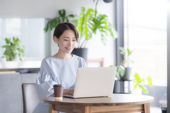 観葉植物のあるオシャレな明るいオフィスでノートパソコンで仕事をする日本人女性 オフィスワーク・ビジネスシーン