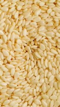 White Sesame Seeds in Motion. Macro view of pale sesame seeds shifting and flowing into an organic granular pattern.