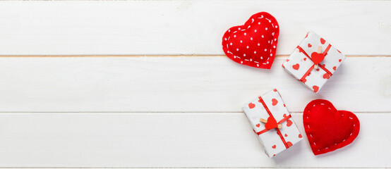 Fototapeta premium Valentine or other holiday handmade present in paper with red hearts and gifts box in holiday wrapper. Present box gift on white wooden table top view with copy space, empty space for design