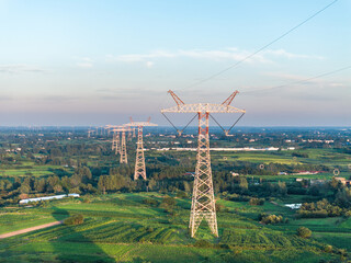 Fototapeta premium High voltage transmission towers aligned across green farmland under clear sky