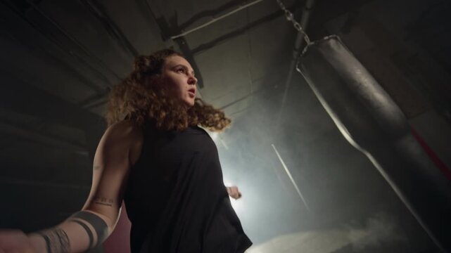 Caucasian young woman skipping rope in dark boxing gym, filmed in slow motion. Perfect for fitness brand advertisements, gym promotional videos, and motivational sports marketing campaigns