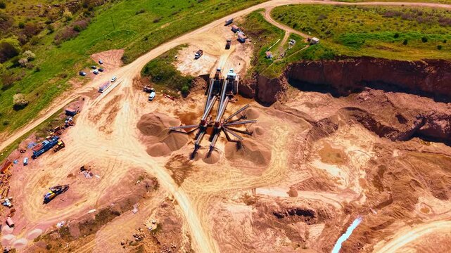 High angle view of sorting machinery and sand stockpiles at stone quarry. Drone view captures conveyor machinery and piles of crushed rock near steep excavation walls in sunlight.
