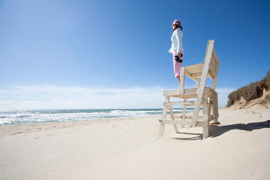 Woman standing on wooden structure on beach and looking out over sea horizon