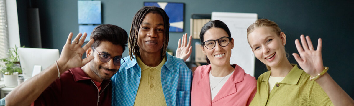 Portrait of diverse young adult coworkers waving at camera during team introduction in office, showing inclusion and collaboration. Ideal for workplace culture, hiring, onboarding