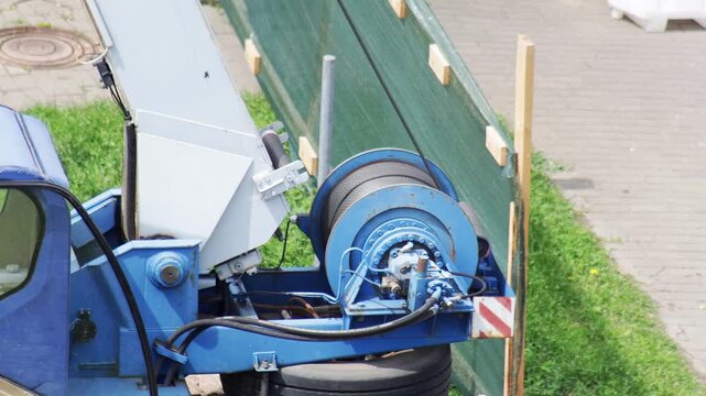 Blue construction crane part with powerful winch system and robust steel cable for lifting heavy objects, industrial machinery detail, slow motion