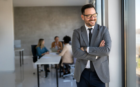 Handsome young business man standing confident in the corporate office in front of his team