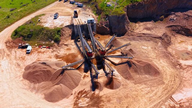 Conveyor belt plant processing gravel and sand in stone quarry. Overhead aerial view of mineral crushing equipment with large brown mounds of aggregate around.