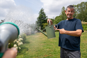 Hosepipe ban. A man points to a watering can as a person uses a hose pipe during a hosepipe ban. Summer drought and water rationing. Water restrictions.  © Steven