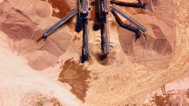 Aerial view of conveyor belts discharging processed material in a quarry. Heavy industrial belts pour crushed stone onto large heaps on the ground.