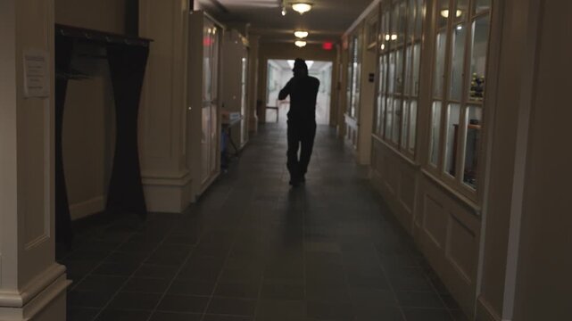 Dark hooded figure carrying a rifle in a school hallway - soft focus 60p