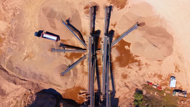 Top down aerial shot of sand sorting conveyor belts and mounds. Industrial machinery separates mineral materials in an open pit mining area.