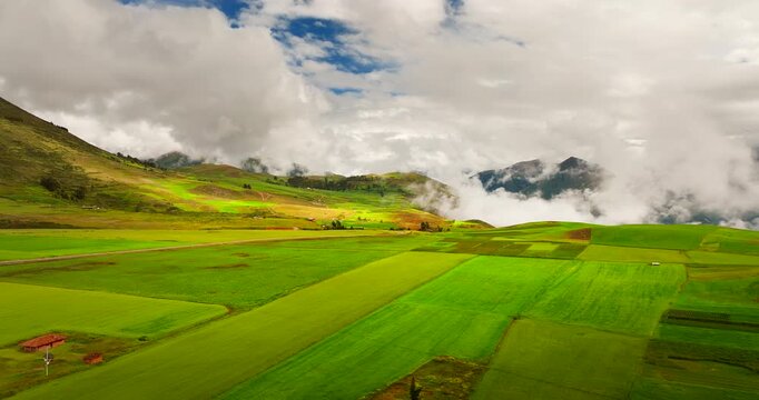 Drone overlooks vibrant farmland in Maras district of Peru Sacred Valley, aerial establishing backdrop with wispy clouds rising from valley