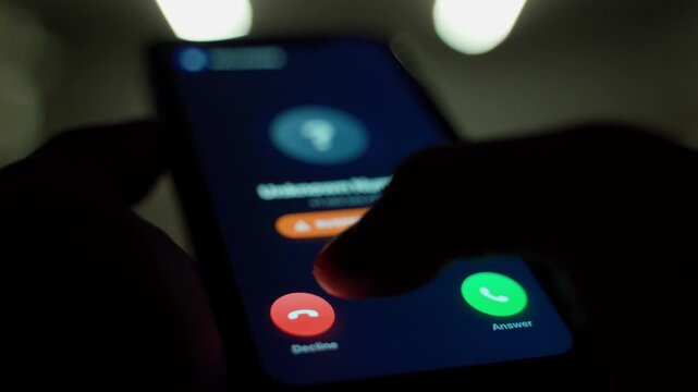 User not answering call from unknown number. Smartphone screen with incoming call from unknown number in the dark 