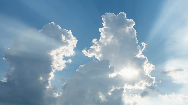 Sun shining through white puffy clouds