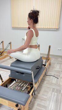 Pilates reformer workout featuring a woman in lotus pose performing upper body strength exercises. Static side profile shot in a modern wellness studio.