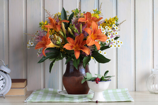 Cozy summer still life with orange daylilies, wildflowers and fresh serviceberries arranged in a rustic country setting