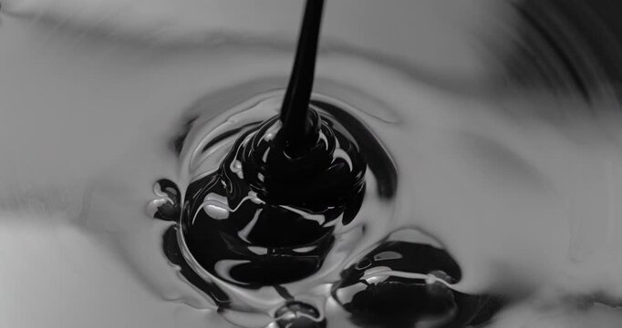 Black Viscous Liquid Pouring. Glossy fluid falls into a reflective pool, creating concentric ripples and swirling abstract forms.