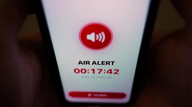 Hand holding smartphone with air raid alert app in the dark close-up 