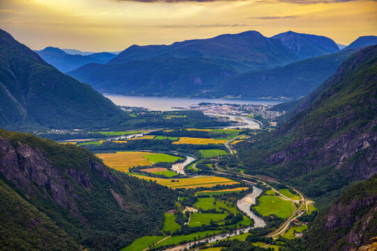 Aerial view from Litlefjellet over Romsdalen Valley, Rauma River, Andalsnes and Romsdalsfjord in Norway, with winding water, farms and mountains at sunset.