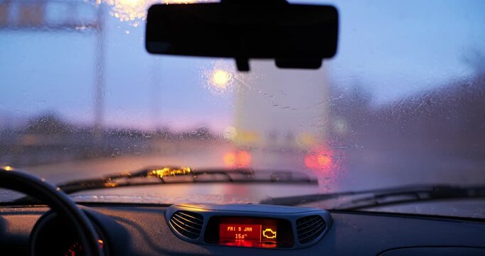 Car driving behind truck on highway in heavy rain at sunset with windshield wipers and colorful twilight bokeh lights