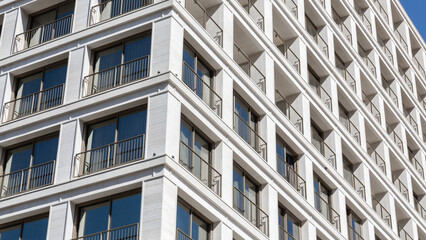 Fototapeta premium Closeup view of modern white apartment building with balconies and reflective glass windows under clear blue sky