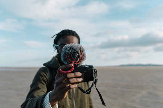 Young traveler making vlog of himself at beach against sky