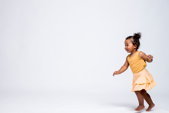 Happy little girl running barefoot in front of grey background