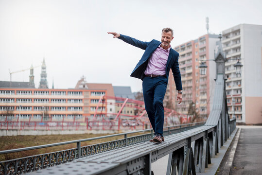 Stylish mature businessman wearing blue suit balancing on railing of bridge