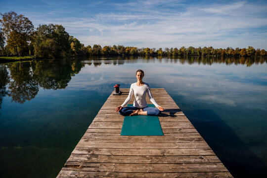 Woman practicing meditation in front of lake on sunny day