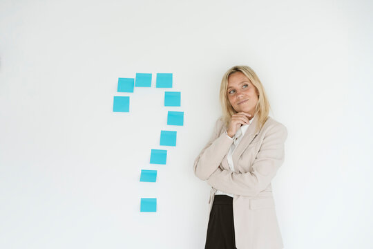 Businesswoman standing next to question mark on the wall