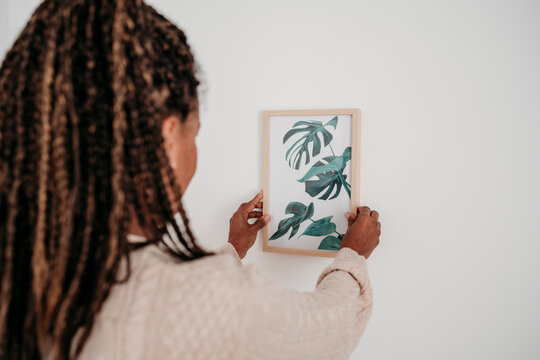 Mature woman hanging picture frame on wall at home